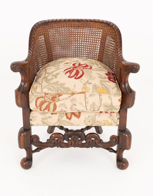 A three-piece Carolean style seating suite comprising a settee and two matching armchairs with woven cane backrests, carved scroll stretchers, and floral fabric seat cushions. View X