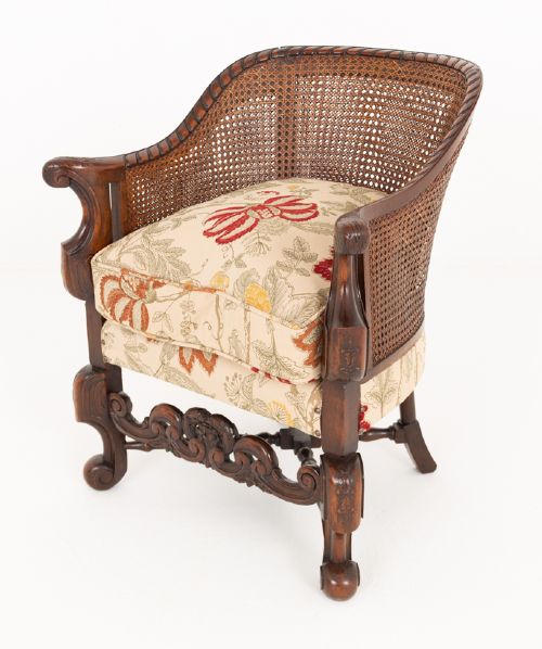A three-piece Carolean style seating suite comprising a settee and two matching armchairs with woven cane backrests, carved scroll stretchers, and floral fabric seat cushions. View XII