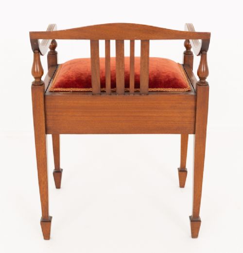 A Sheraton Revival mahogany piano stool featuring a slatted curved backrest, curved arms, red velvet cushioned seat, and square tapered legs with inlaid boxwood stringing. View IV