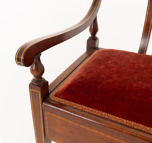 A Sheraton Revival mahogany piano stool featuring a slatted curved backrest, curved arms, red velvet cushioned seat, and square tapered legs with inlaid boxwood stringing. View VII