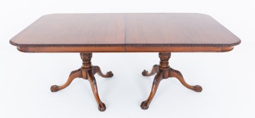 fig 1. A Regency Revival twin-pedestal mahogany dining table featuring carved edging, turned support pillars, and splayed legs ending in carved feet.