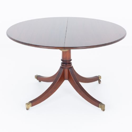 fig 1. An extendable Regency Revival oval mahogany dining table with a central turned pedestal support, four reeded swept legs, and brass castors.
