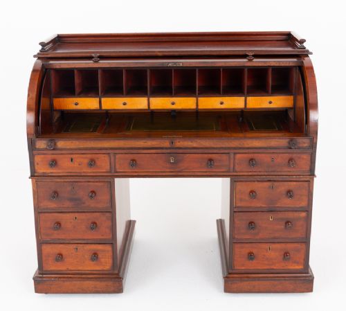 fig 2. A Victorian mahogany cylinder desk featuring a curved roll-top hood, multiple pedestal drawers, and turned wooden knobs.