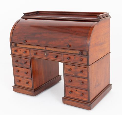 A Victorian mahogany cylinder desk featuring a curved roll-top hood, multiple pedestal drawers, and turned wooden knobs. View VII