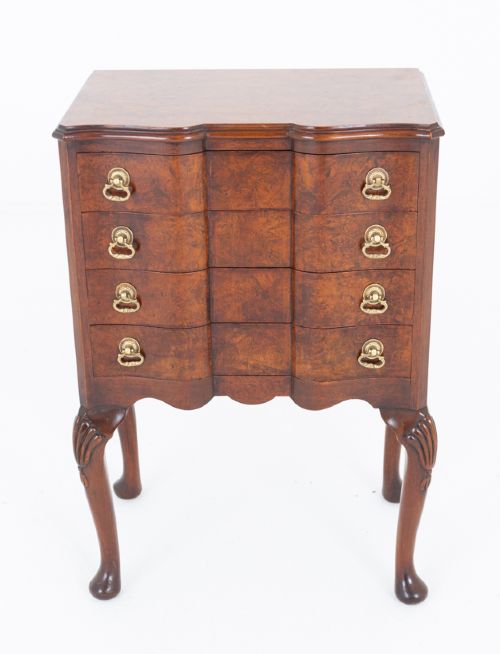 fig 1. A Queen Anne style burr walnut bedside chest featuring four drawers with brass drop handles, a contoured front, and carved cabriole legs with pad feet.