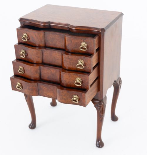 A Queen Anne style burr walnut bedside chest featuring four drawers with brass drop handles, a contoured front, and carved cabriole legs with pad feet. View IV