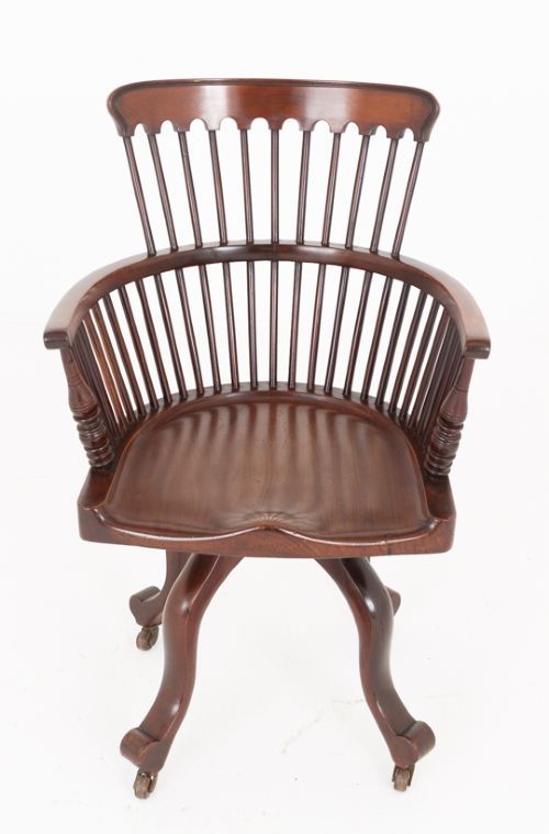fig 1. Victorian mahogany swivel desk chair featuring a spindle back, rounded armrests, contoured wooden saddle seat, and splayed legs with castors.