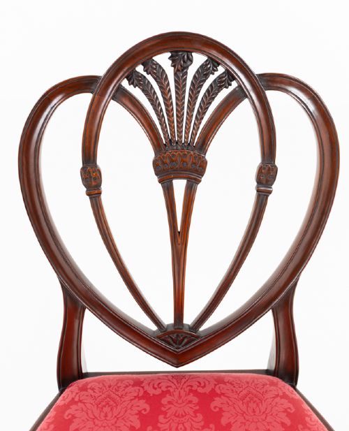 A set of twelve mahogany dining chairs with carved Prince of Wales plume backs and red damask fabric seats arranged in a arc. View IV