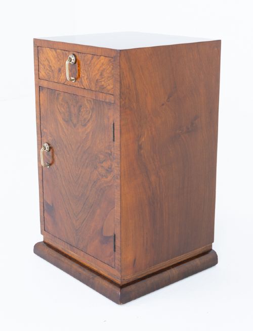 An Art Deco burr walnut bedside cabinet featuring a single upper drawer above a lower cupboard door with brass pull handles. View IV