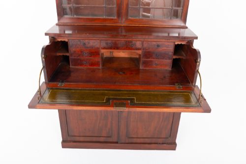 fig 2. A William IV mahogany secretaire bookcase featuring an upper cabinet with astragal glazed doors, a pull-down secretaire drawer with brass lion mask handles, and a lower two-door cupboard.
