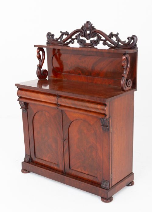 A nineteenth-century Victorian mahogany chiffonier featuring a carved crest backboard, a raised shelf with scrolled supports, a cushion drawer, two panelled doors, and bun feet. View VIII