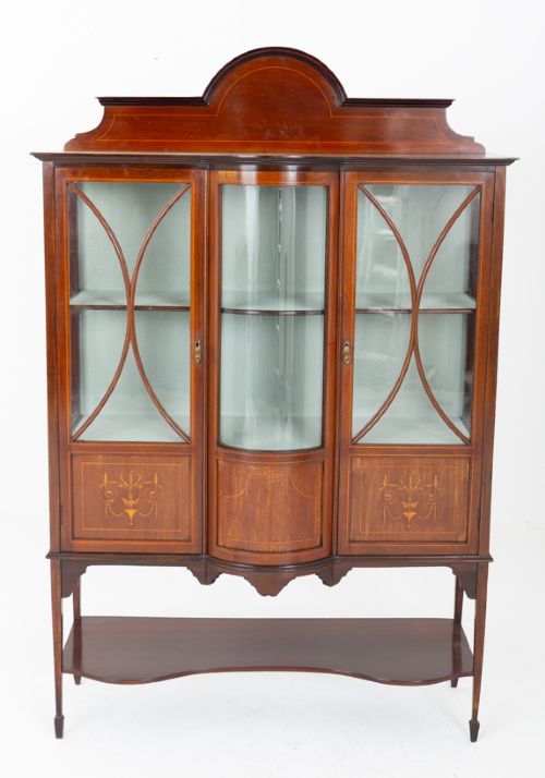 fig 1. A Sheraton Revival mahogany display cabinet featuring an arched pediment, glass-front doors with geometric glazing bars, marquetry inlay panels, and a lower shelf supported by slender legs.