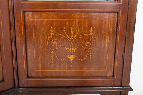 fig 2. A Sheraton Revival mahogany display cabinet featuring an arched pediment, glass-front doors with geometric glazing bars, marquetry inlay panels, and a lower shelf supported by slender legs.