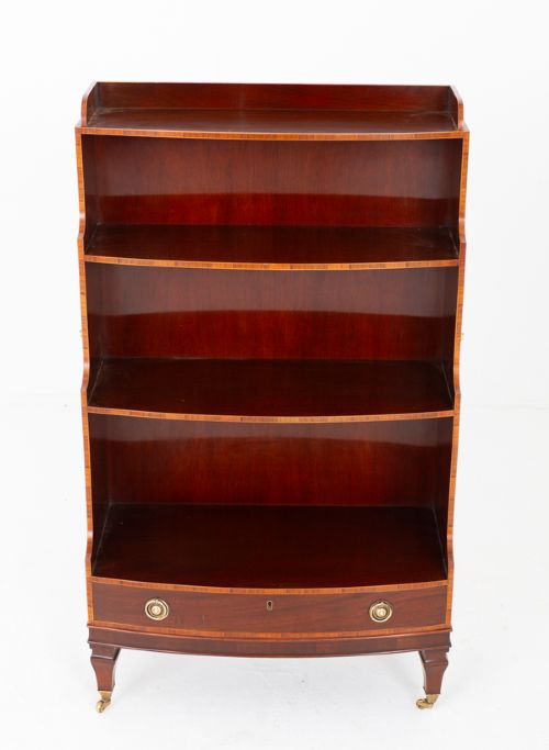 fig 1. A dark mahogany waterfall bookcase with four graduated open shelves, brass side handles, and a bow-front lower drawer on turned legs with castors.