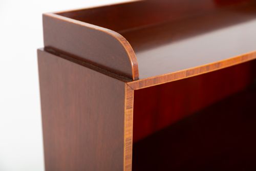 fig 2. A dark mahogany waterfall bookcase with four graduated open shelves, brass side handles, and a bow-front lower drawer on turned legs with castors.