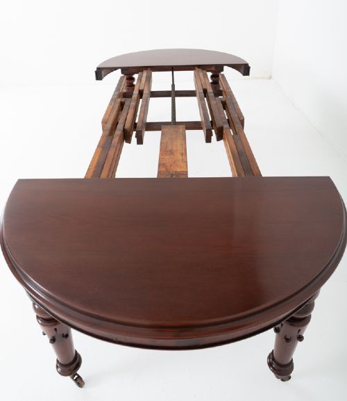 A William IV mahogany extending dining table with turned carved legs and brass castors set against a plain white background. View V