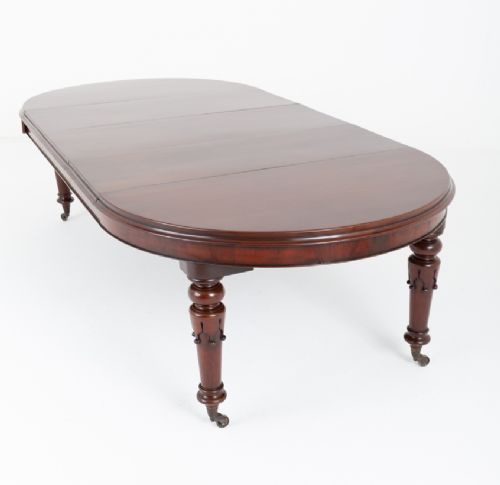 A William IV mahogany extending dining table with turned carved legs and brass castors set against a plain white background. View VII