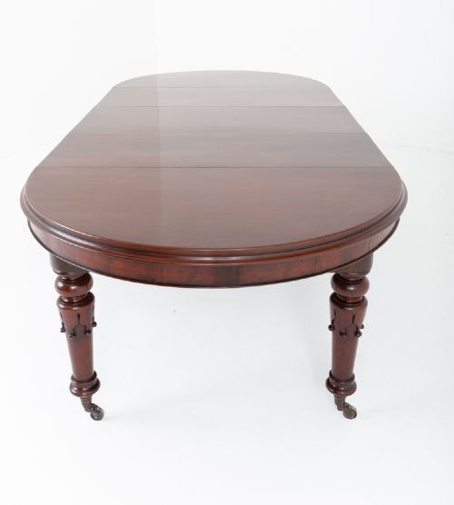 A William IV mahogany extending dining table with turned carved legs and brass castors set against a plain white background. View IX