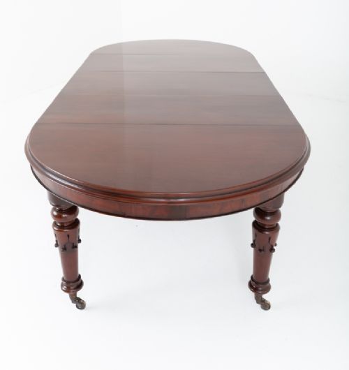 A William IV mahogany extending dining table with turned carved legs and brass castors set against a plain white background. View X