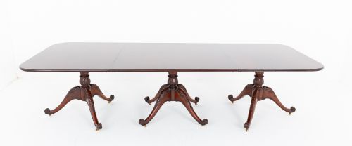 fig 1. A large Regency style dark mahogany dining table featuring a three-pedestal base with carved splayed legs resting on brass castors.