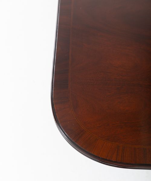 fig 2. A large Regency style dark mahogany dining table featuring a three-pedestal base with carved splayed legs resting on brass castors.