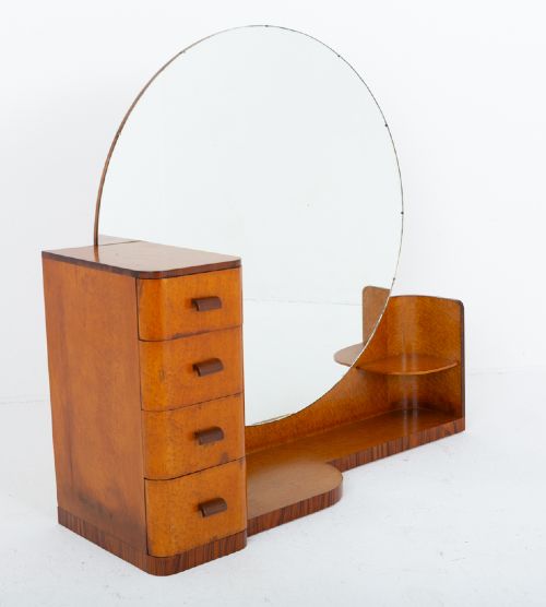 fig 1. An asymmetric Art Deco dressing table featuring warm birds eye maple veneer, a large circular mirror, a four-drawer stack on the left, and tiered open shelving on the right.