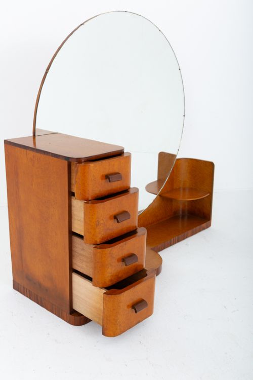 fig 2. An asymmetric Art Deco dressing table featuring warm birds eye maple veneer, a large circular mirror, a four-drawer stack on the left, and tiered open shelving on the right.