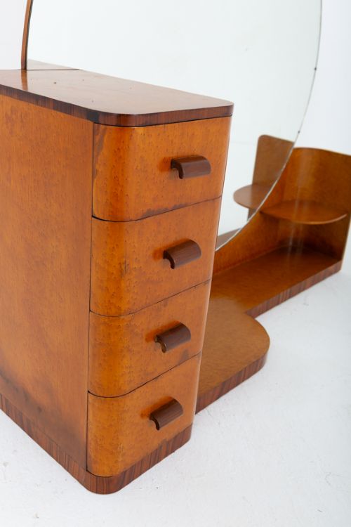 An asymmetric Art Deco dressing table featuring warm birds eye maple veneer, a large circular mirror, a four-drawer stack on the left, and tiered open shelving on the right. View IV