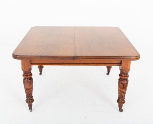 fig 1. A Victorian blonde oak extending dining table featuring rounded corners, turned spiral-fluted legs, and brass castors against a white background.
