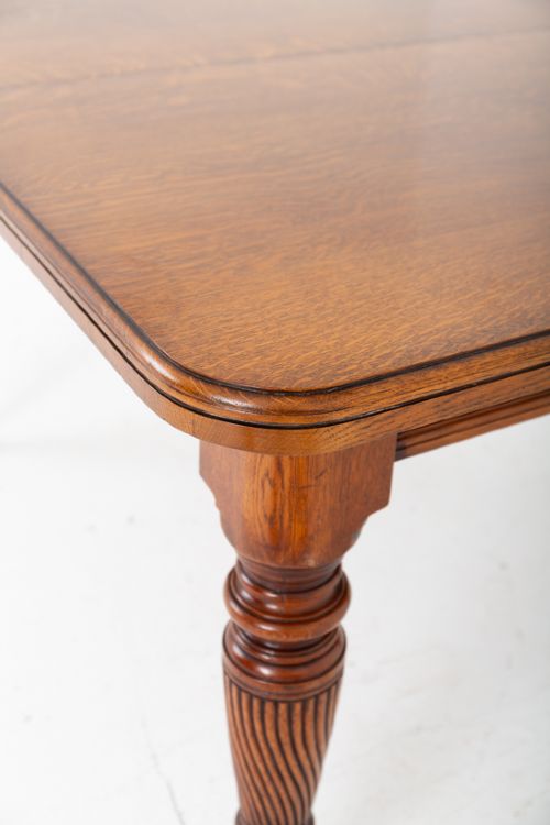 fig 2. A Victorian blonde oak extending dining table featuring rounded corners, turned spiral-fluted legs, and brass castors against a white background.