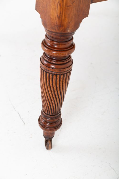 A Victorian blonde oak extending dining table featuring rounded corners, turned spiral-fluted legs, and brass castors against a white background. View IV