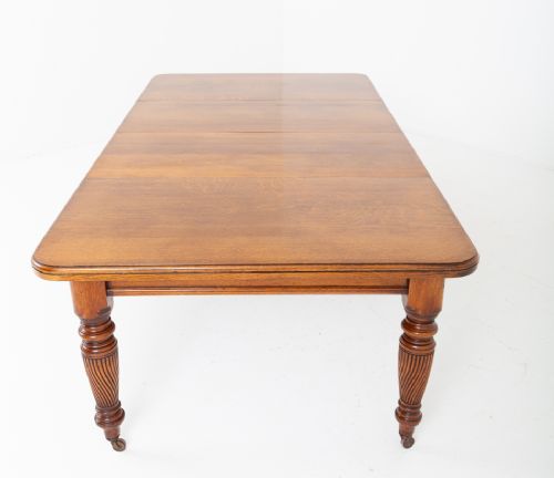 A Victorian blonde oak extending dining table featuring rounded corners, turned spiral-fluted legs, and brass castors against a white background. View VII