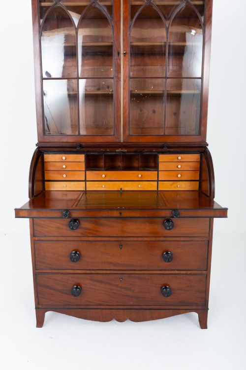 fig 2. A Regency mahogany cylinder bureau bookcase featuring Gothic astragal glazed upper doors above a curved roll-top desk and three long drawers with turned dark handles.