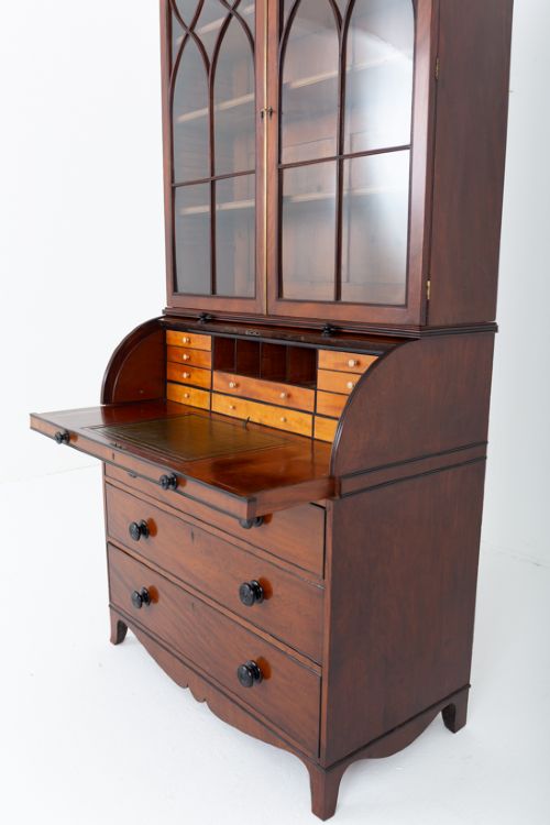 fig 3. A Regency mahogany cylinder bureau bookcase featuring Gothic astragal glazed upper doors above a curved roll-top desk and three long drawers with turned dark handles.
