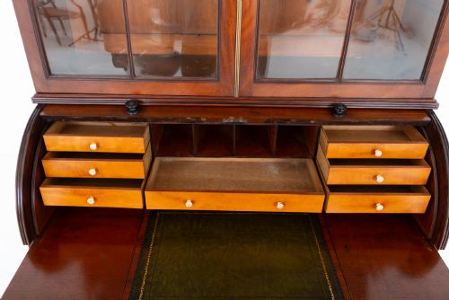 fig 4. A Regency mahogany cylinder bureau bookcase featuring Gothic astragal glazed upper doors above a curved roll-top desk and three long drawers with turned dark handles.