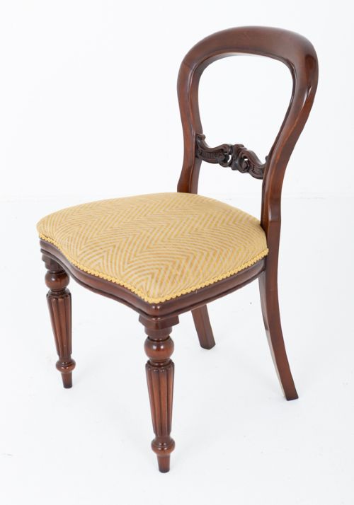 A set of eight Victorian style mahogany dining chairs with rounded balloon backs, carved mid-rails, gold upholstered seats, and fluted front legs. View V
