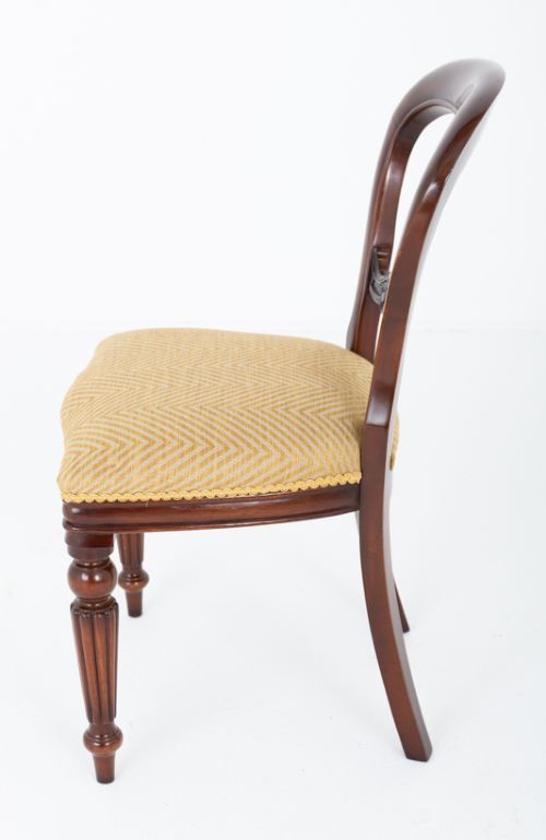 A set of eight Victorian style mahogany dining chairs with rounded balloon backs, carved mid-rails, gold upholstered seats, and fluted front legs. View VI