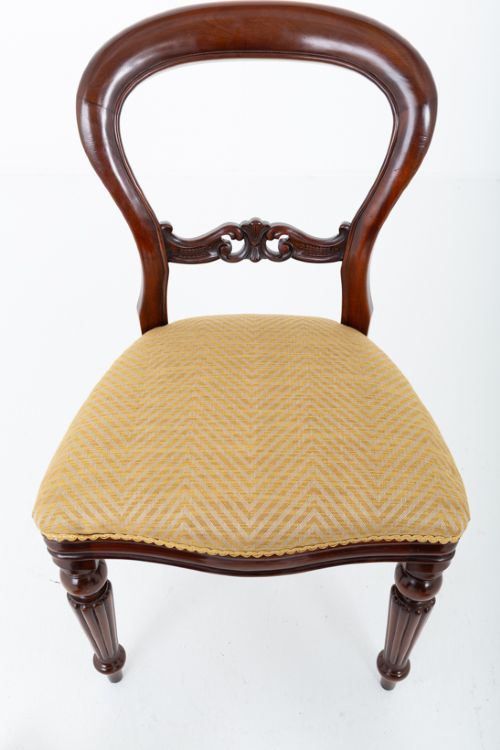 A set of eight Victorian style mahogany dining chairs with rounded balloon backs, carved mid-rails, gold upholstered seats, and fluted front legs. View VIII