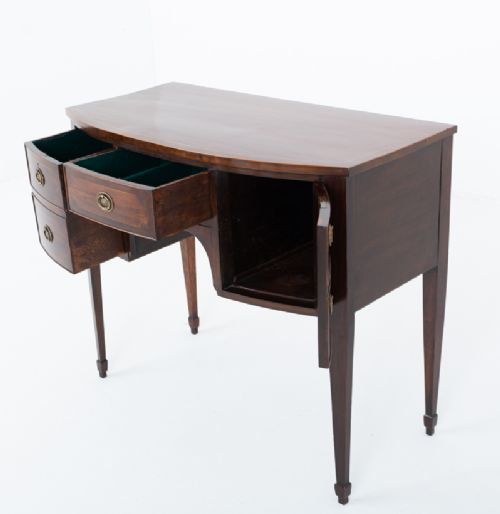 An antique Georgian bow-fronted mahogany sideboard with drawers featuring brass oval drop handles and tapered square legs. View VI