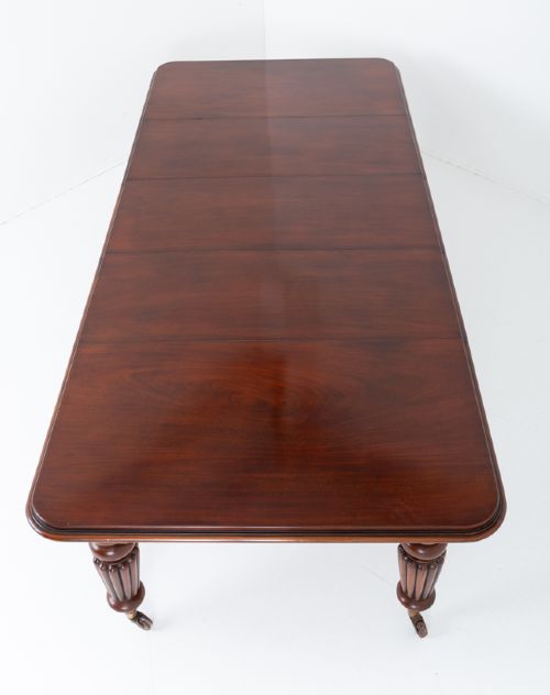 A William IV mahogany extending dining table with three additional leaves, standing on turned and reeded legs with brass castors. View X