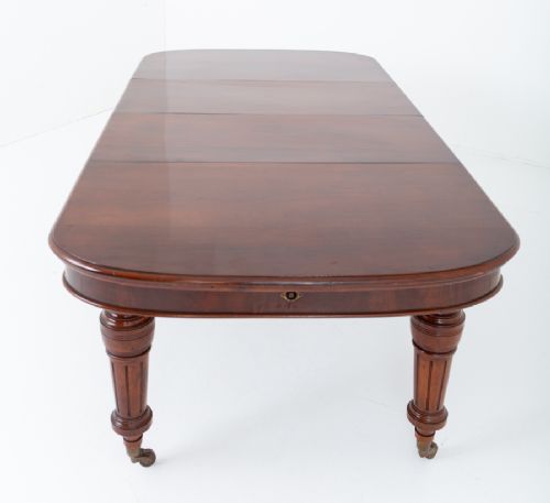 A Victorian mahogany extending dining table with two removable extension leaves, turned fluted legs, and brass castors. View VII
