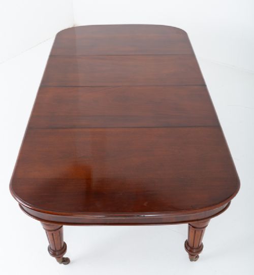 A Victorian mahogany extending dining table with two removable extension leaves, turned fluted legs, and brass castors. View VIII