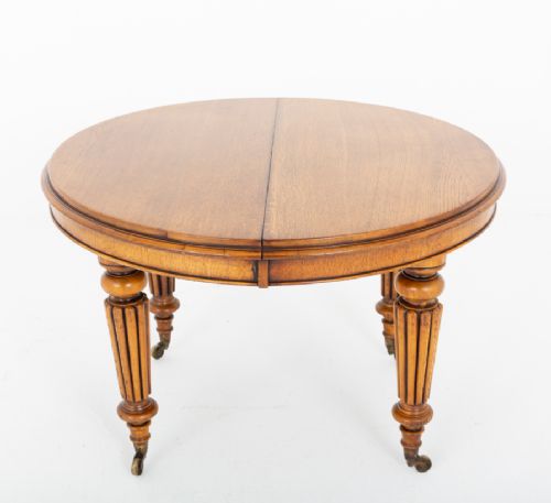 A Victorian blonde oak extending dining table featuring turned fluted legs supported on metal castors. View II