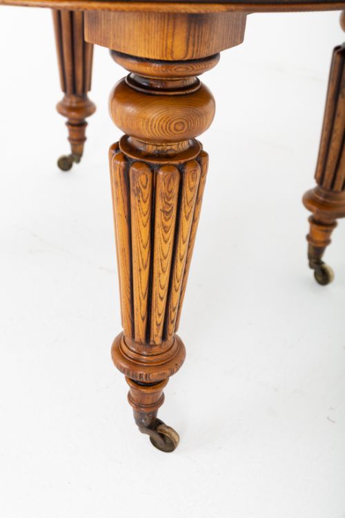 A Victorian blonde oak extending dining table featuring turned fluted legs supported on metal castors. View III