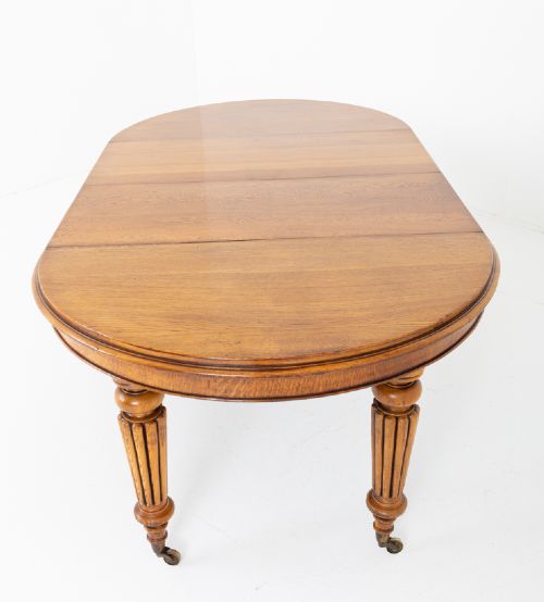 A Victorian blonde oak extending dining table featuring turned fluted legs supported on metal castors. View VI