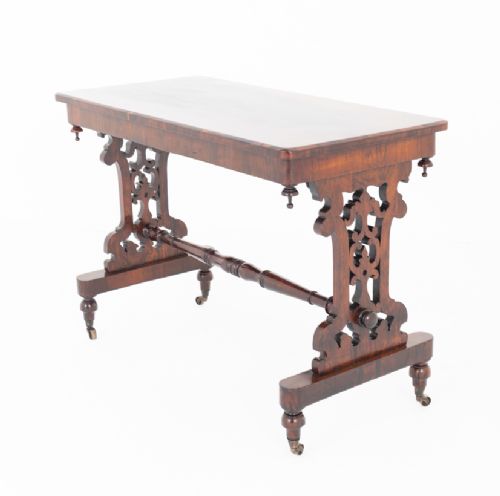 A mid-19th century Victorian rosewood stretcher table featuring a rectangular polished top, openwork pierced end supports, a turned central stretcher, and brass castors. View III