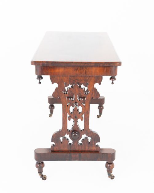 A mid-19th century Victorian rosewood stretcher table featuring a rectangular polished top, openwork pierced end supports, a turned central stretcher, and brass castors. View VII