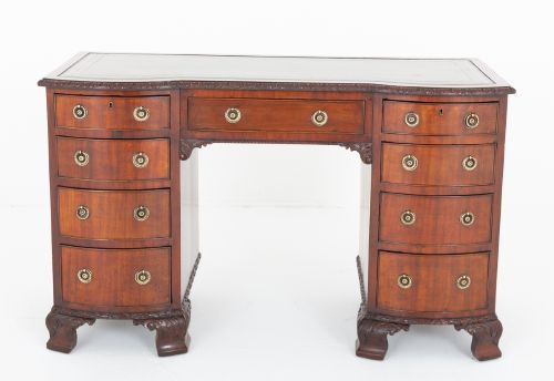 fig 1. A Georgian Revival mahogany pedestal desk featuring a leather-lined top, curved drawer fronts with brass ring handles, and carved bracket feet.