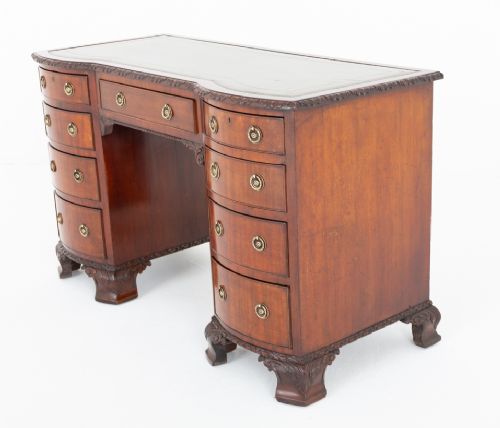 A Georgian Revival mahogany pedestal desk featuring a leather-lined top, curved drawer fronts with brass ring handles, and carved bracket feet. View X