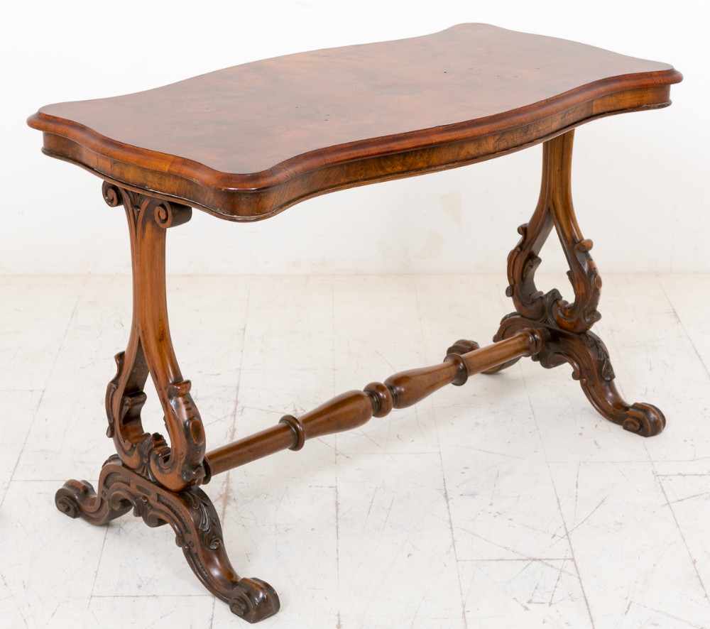 A Victorian burr walnut stretcher table featuring a serpentine top, carved end supports, and a turned central stretcher bar.